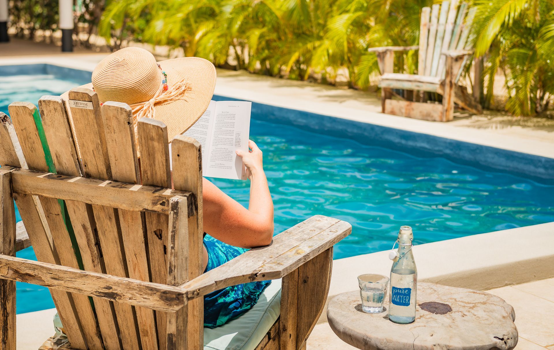 A woman is laying on the edge of a swimming pool wearing a straw hat.