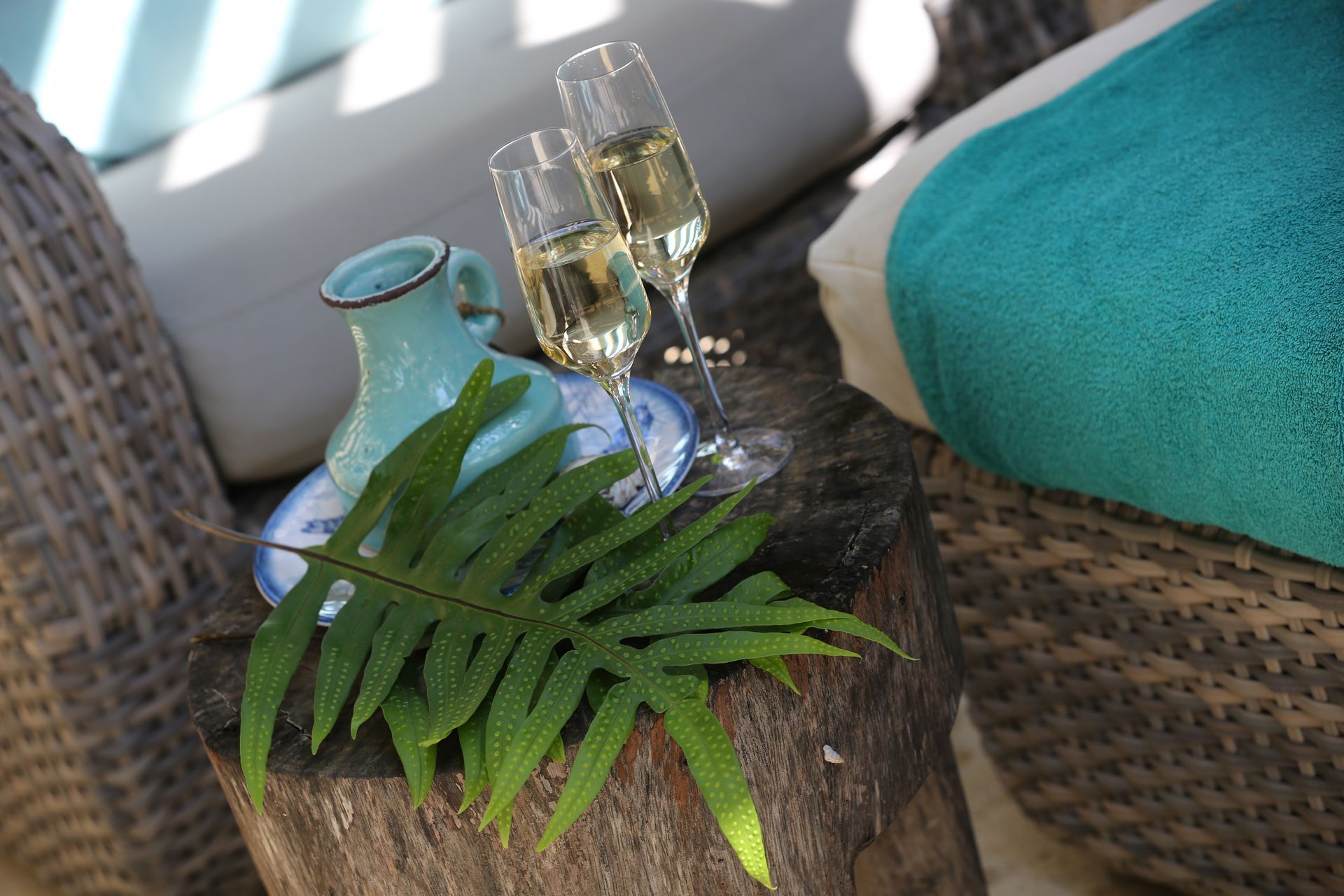 Two glasses of champagne are sitting on a wooden table next to a vase and fern leaves.