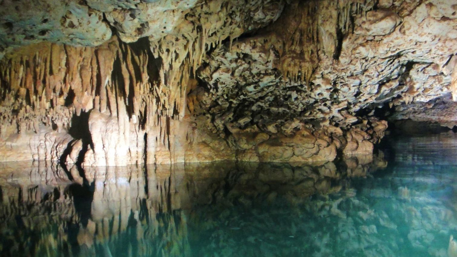 A man is standing in a cave next to a body of water.