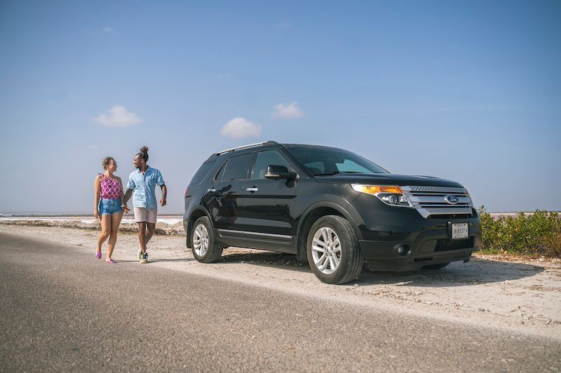 A man and a woman are walking next to a black suv on the side of the road.