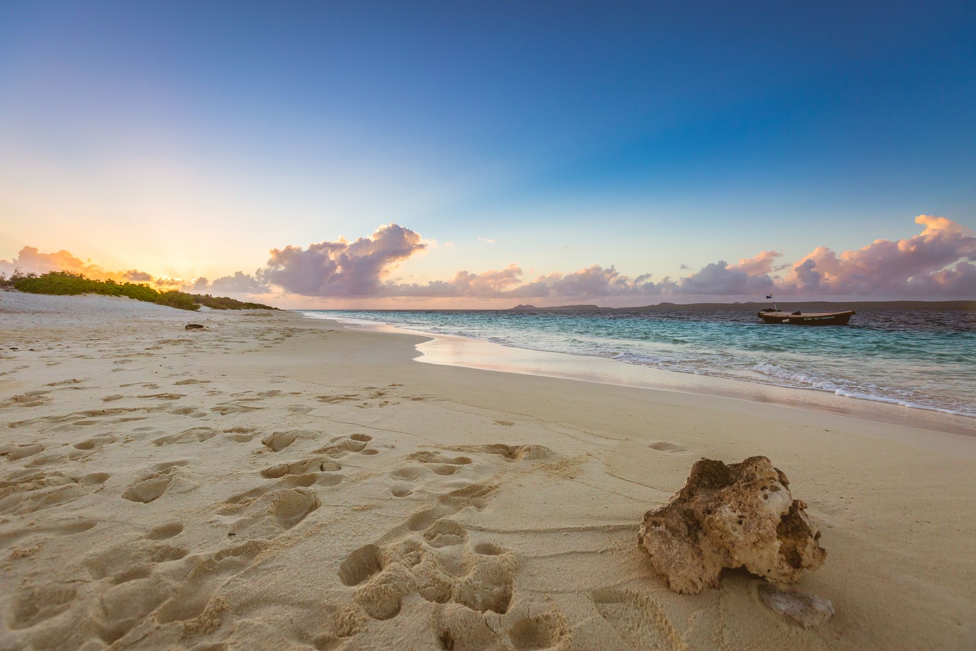 A sandy beach with a boat in the distance at sunset.