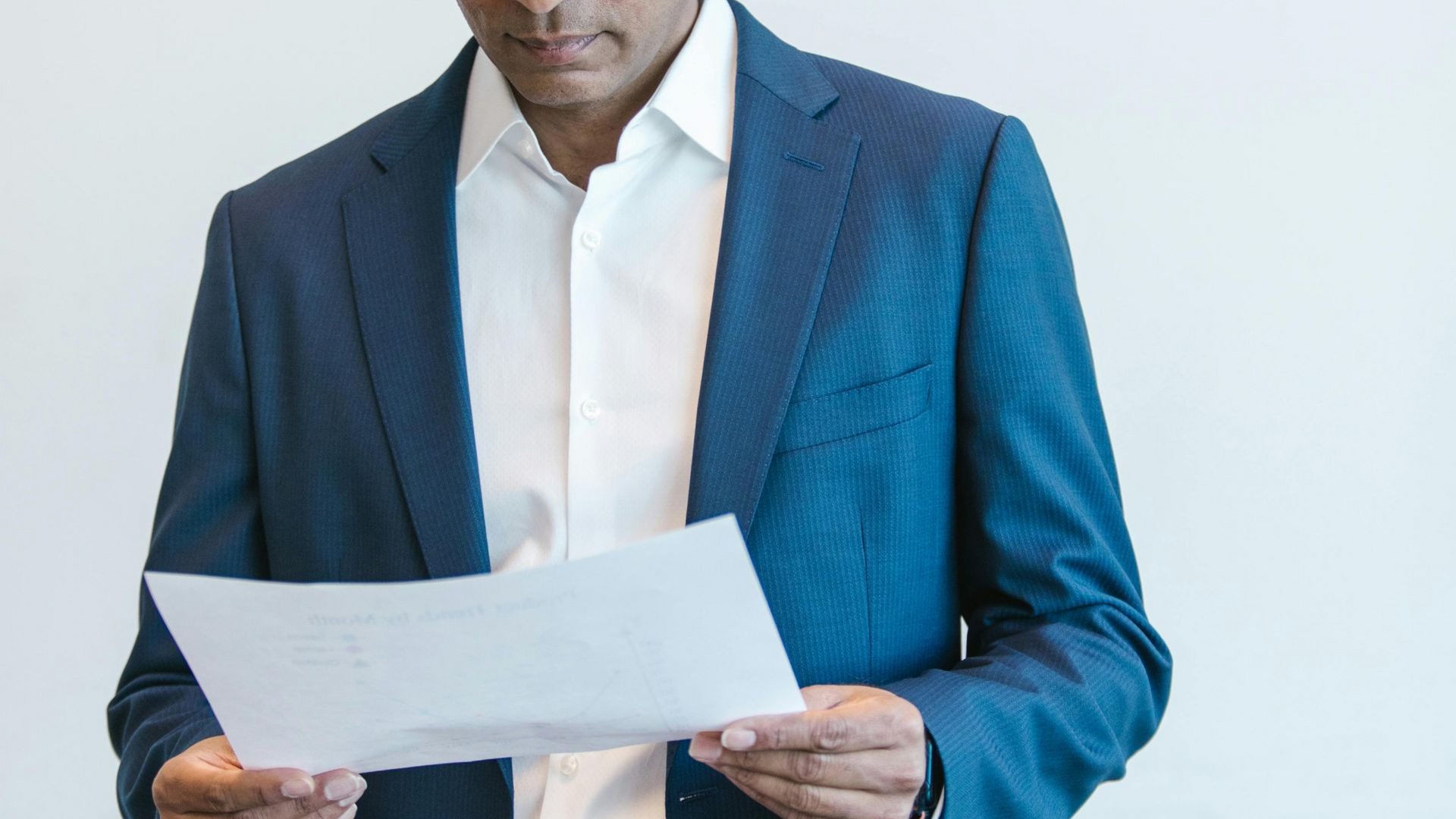 Man in blue blazer and white shirt, reading papers indoors.