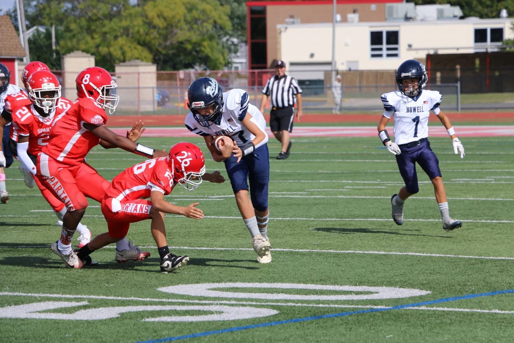Football game: player in blue uniform running with ball, pursued by red team players on a green field.