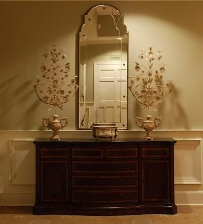 A dark wooden sideboard with a large mirror and decorative items, including sconces and vases, against a pale green wall.