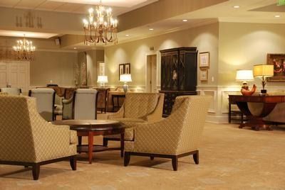 A well-lit, comfortable lounge with armchairs arranged around a table, lit by chandeliers and table lamps.