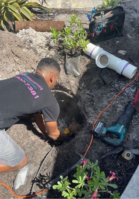 A man is kneeling down in the dirt working on a pipe.