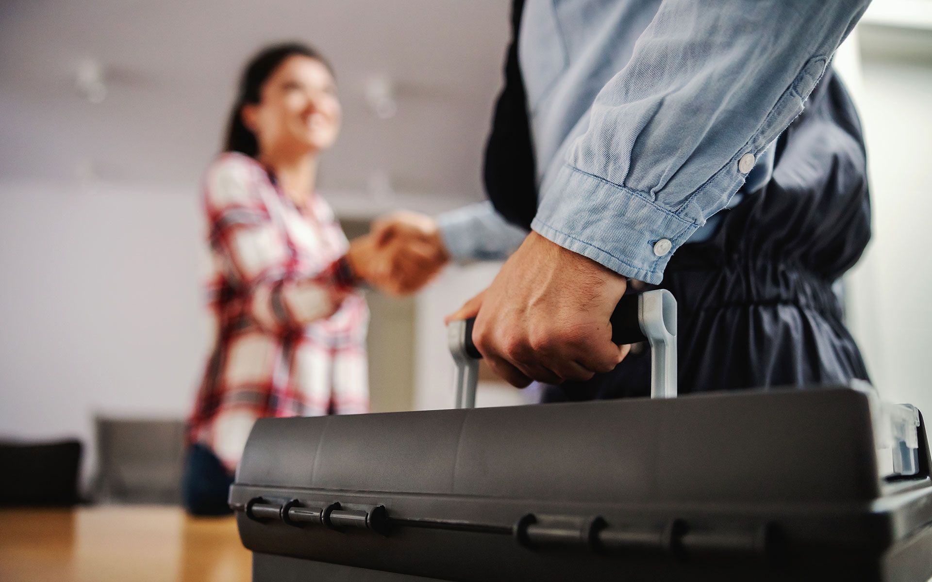 A man is holding a toolbox and shaking hands with a woman.