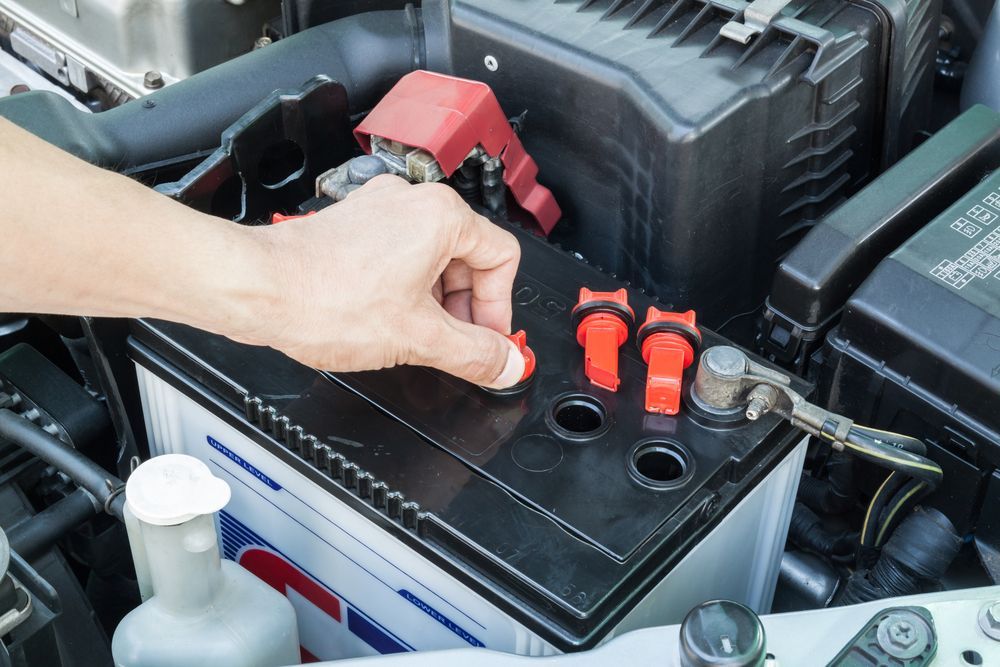 A Hand Unscrewing A Red Filler Cap On A Black Car Battery — AWS Mechanical in Stuart Park, NT