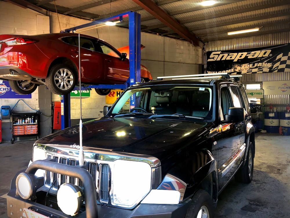 A Jeep is Sitting on a Lift in a Garage Next to a Red Car — AWS Mechanical in Stuart Park, NT