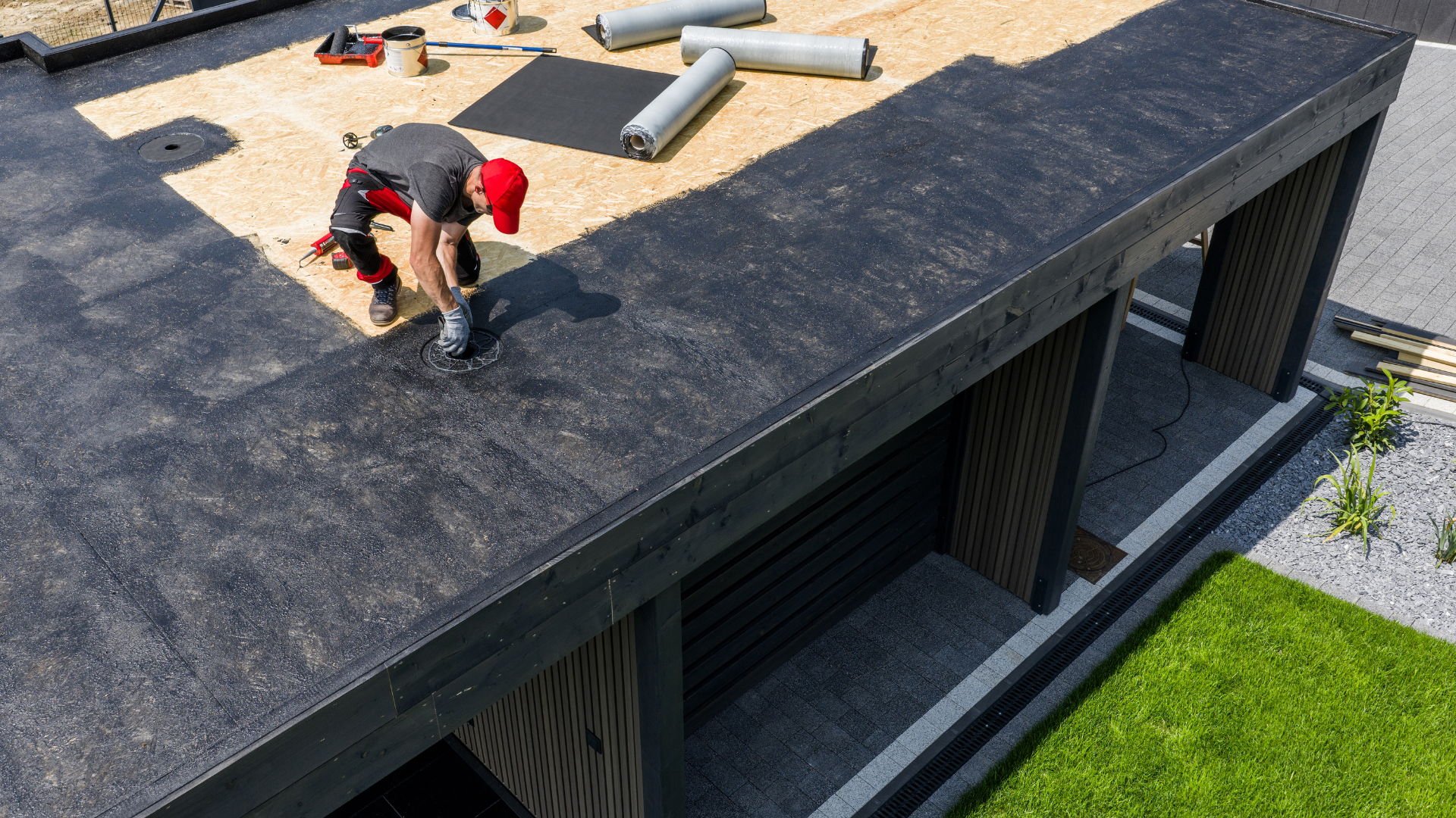 Person working on a black shingle roof of a house with skylights and vents.