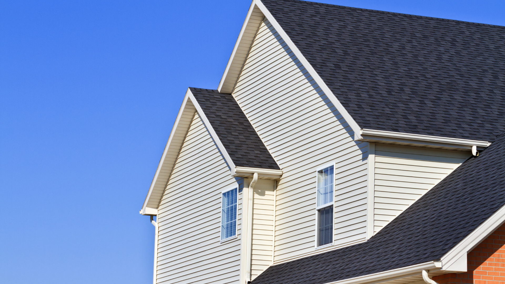 Suburban house with light siding and dark shingled roof against a clear blue sky