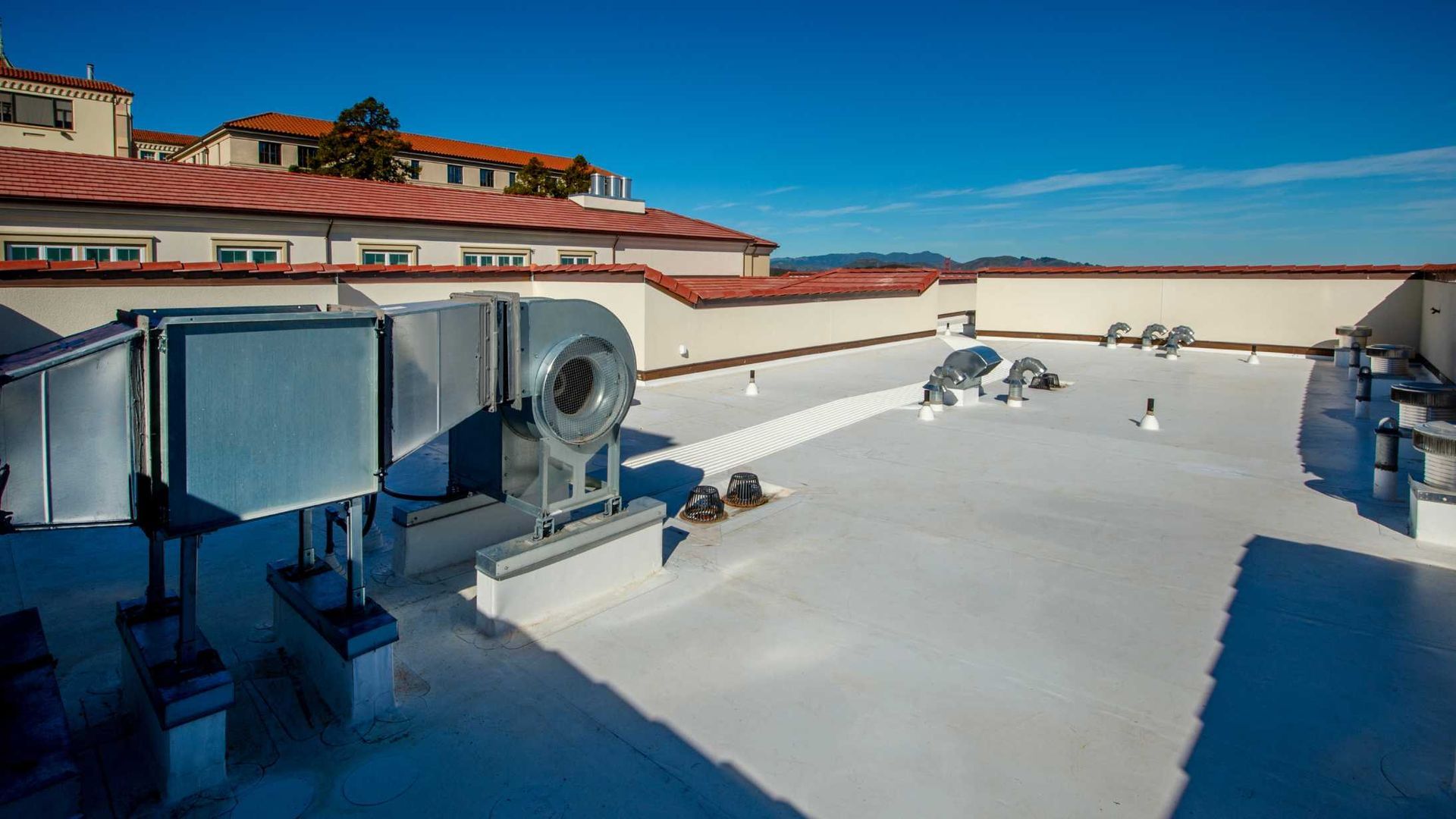 Rooftop with HVAC units and vents under a clear blue sky, surrounded by white parapet walls.