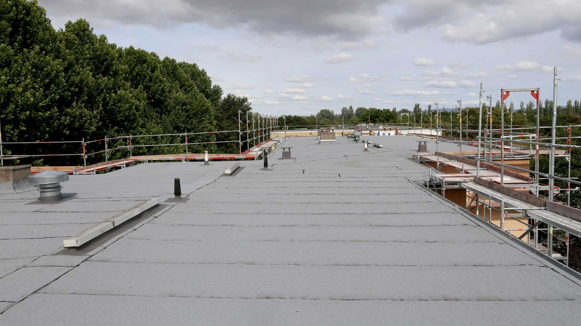 Flat roof under construction with gray insulation panels, scaffolding, and trees in the background