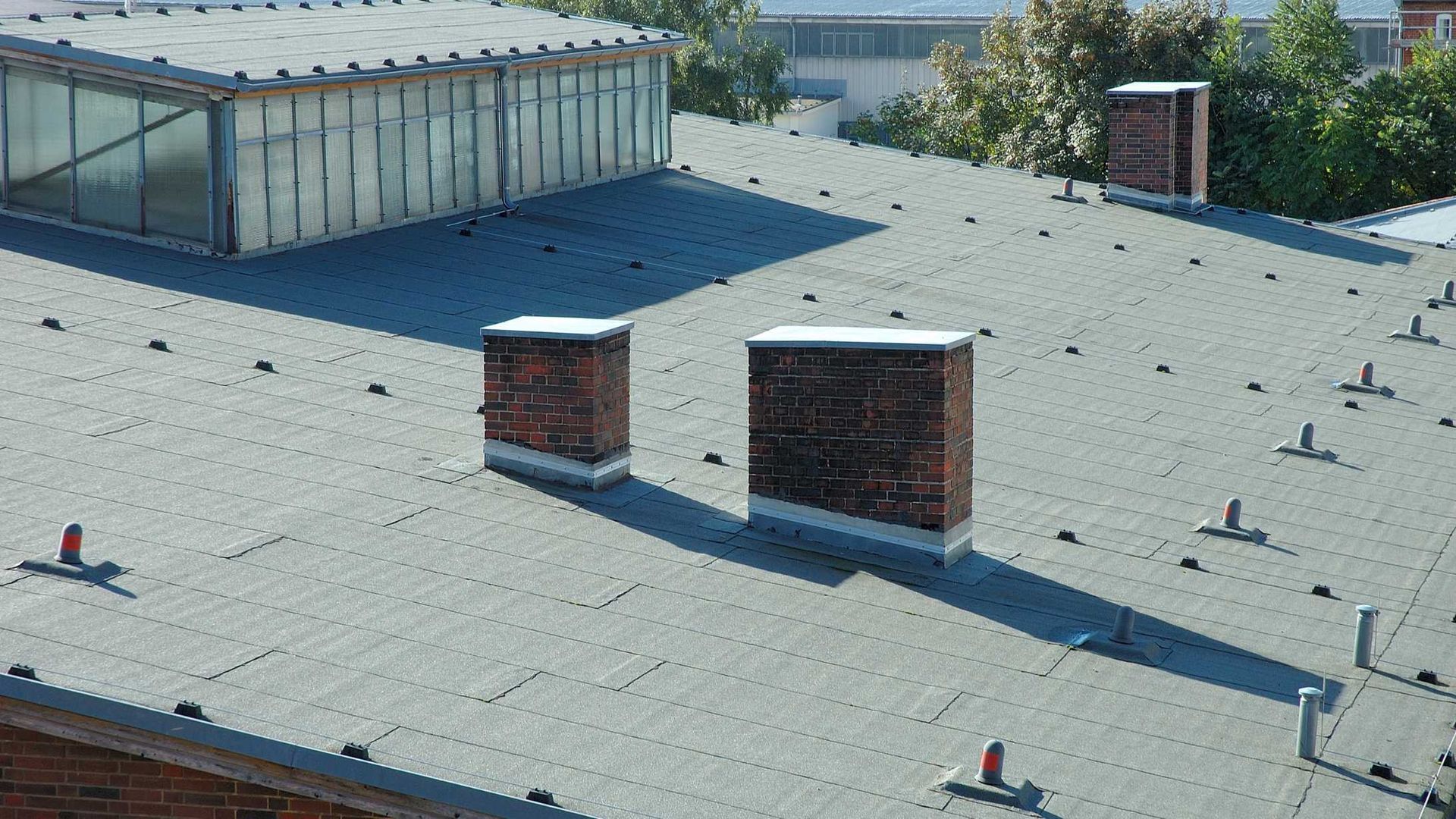 Flat rooftop with light gray gravel, two brick chimneys, and a glass skylight enclosure.