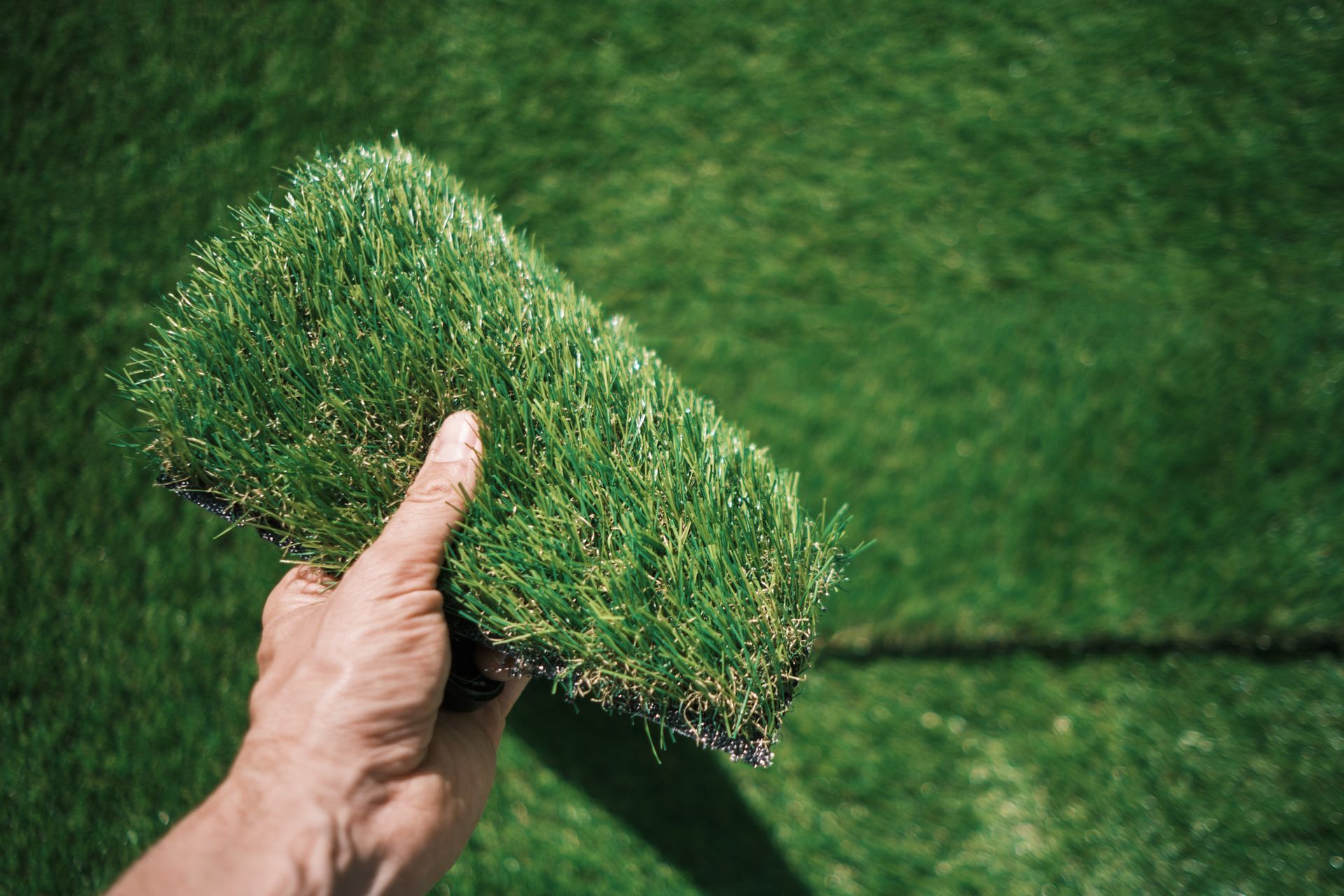 A person is holding a piece of artificial grass in their hand.
