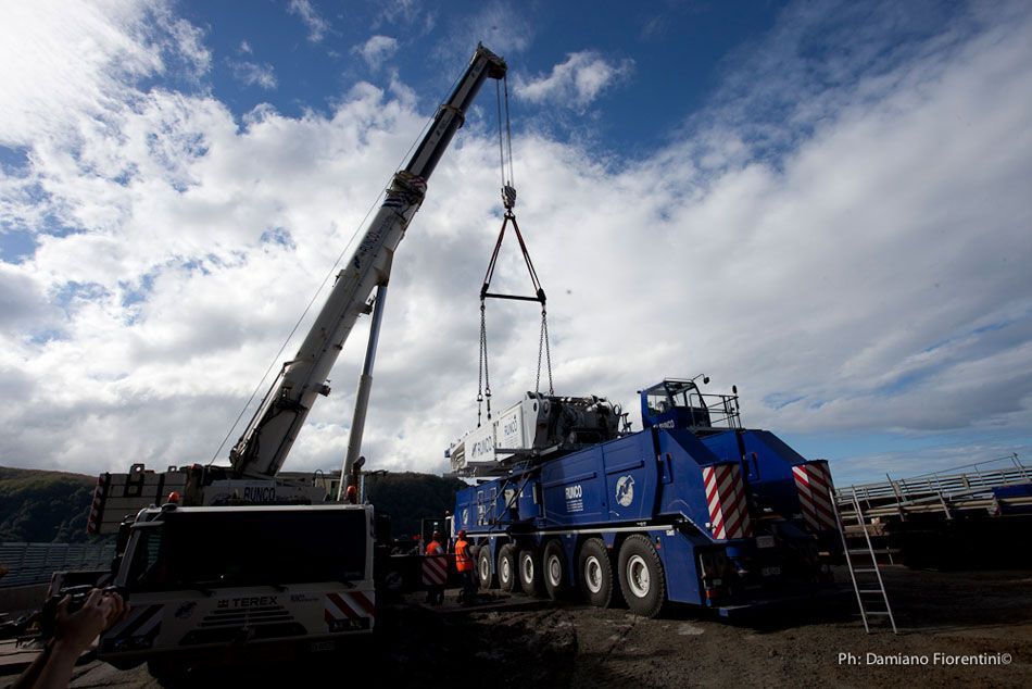 Una grande gru sta sollevando un oggetto di grandi dimensioni da un camion.