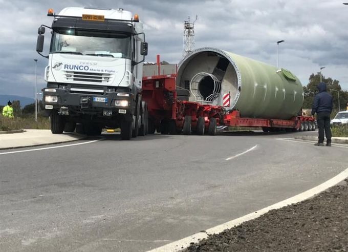 Un camion trasporta un grosso cilindro lungo una strada.