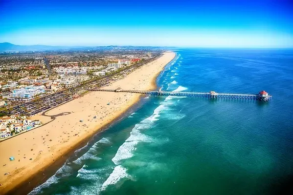An aerial view of a beach with a pier in the middle of the ocean.