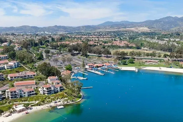 An aerial view of a lake with houses and mountains in the background.