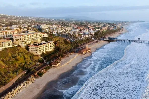 An aerial view of a beach with a pier in the background.