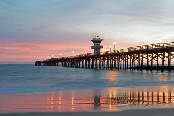 A pier leading into the ocean at sunset with a lifeguard tower.