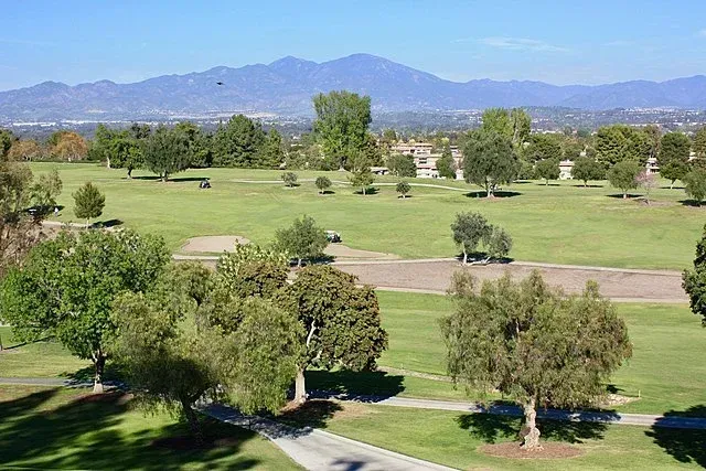 An aerial view of a golf course with trees and mountains in the background.