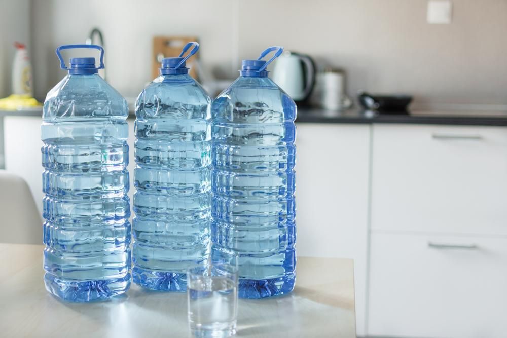Three Large Blue Water Bottles and a Glass of Water on a Kitchen Table — Port Macquarie Pure Water In Wauchope, NSW