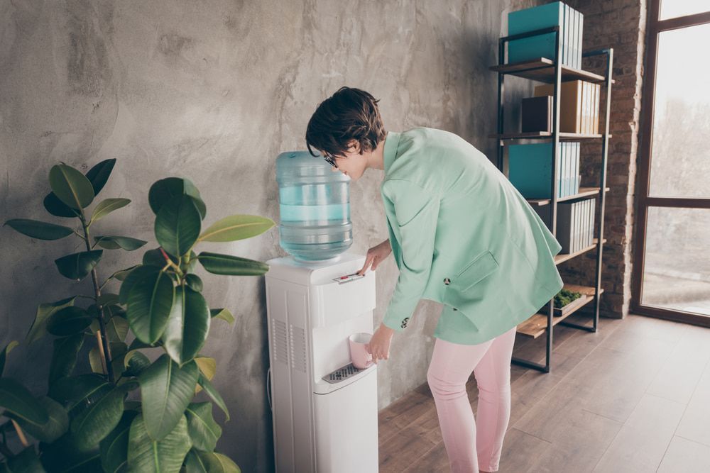 Woman in Green Jacket and Pink Pants Using Water Cooler in Office — Port Macquarie Pure Water In Port Macquarie, NSW