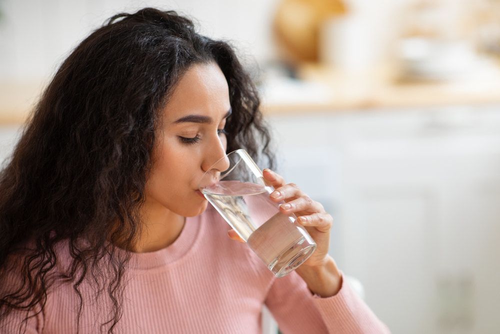 Woman With Curly Dark Hair Drinks Water From a Glass — Port Macquarie Pure Water In Port Macquarie, NSW