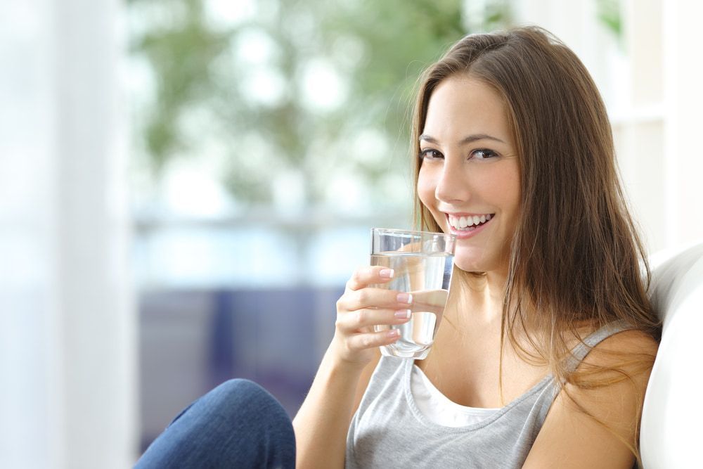 Woman Smiling While Drinking Water, Seated Indoors — Port Macquarie Pure Water In Port Macquarie, NSW