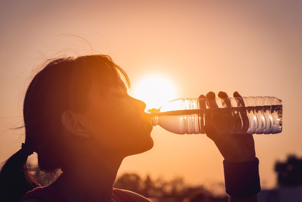 Woman Drinking Water From a Plastic Bottle in Front of the Setting Sun — Port Macquarie Pure Water In Port Macquarie, NSW