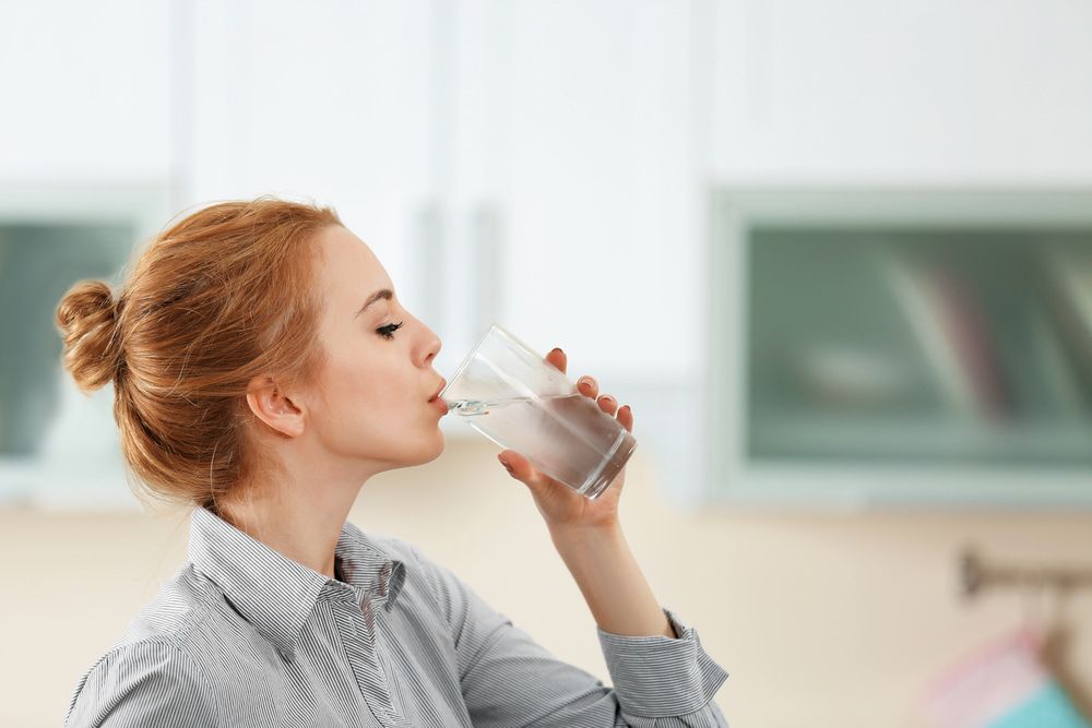 Woman With Red Hair Drinks Water From a Glass in a Bright Kitchen — Port Macquarie Pure Water In Kempsey, NSW