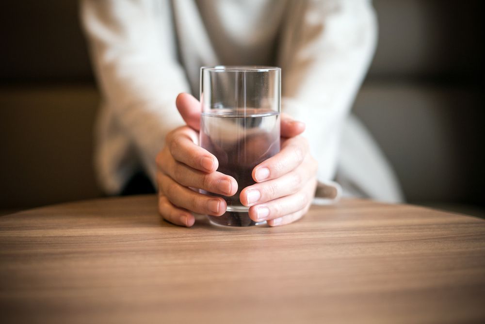 Person Holding a Glass of Water on a Wooden Table — Port Macquarie Pure Water In Port Macquarie, NSW
