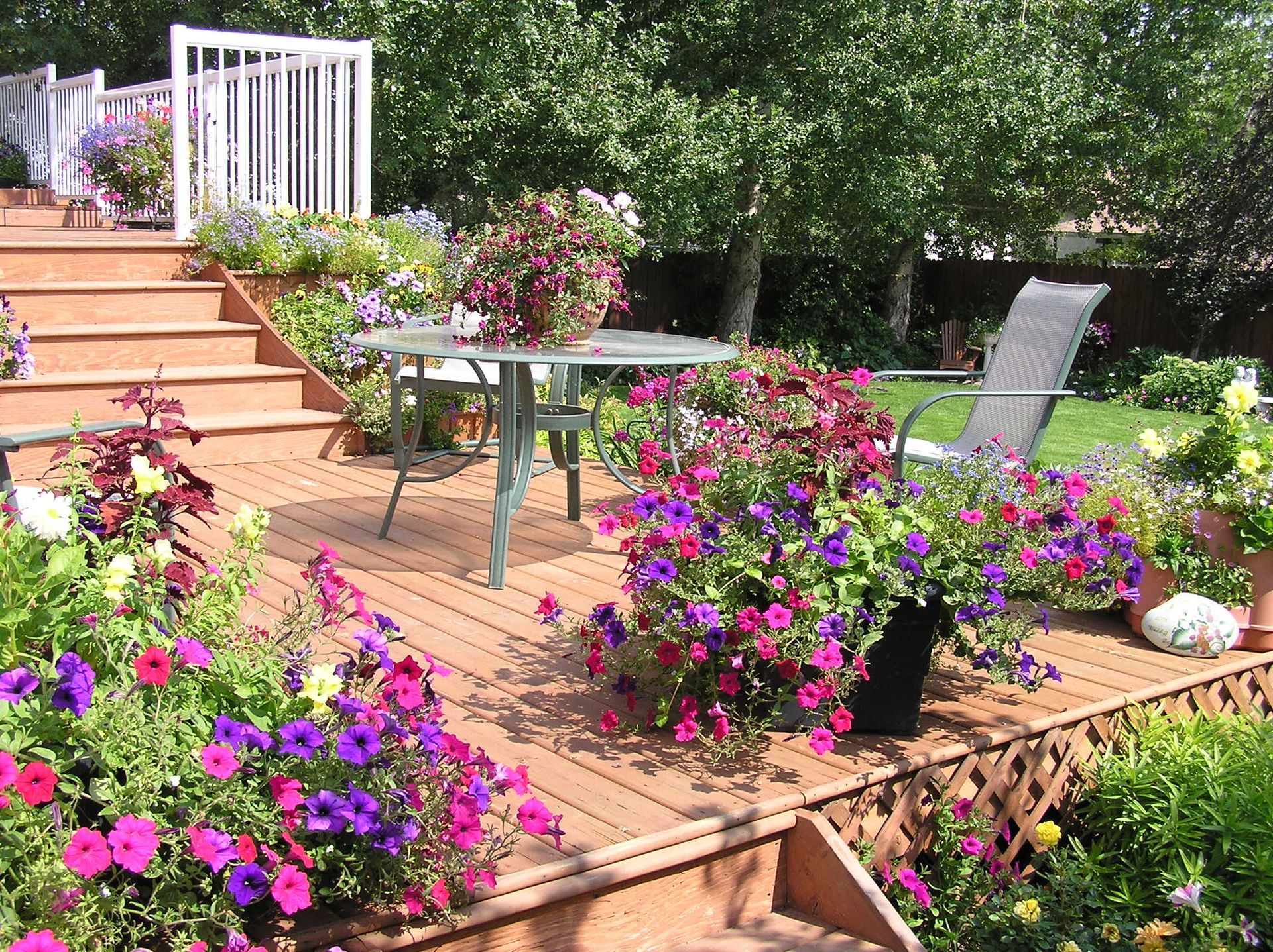 A deck with a table and chairs surrounded by purple and pink flowers