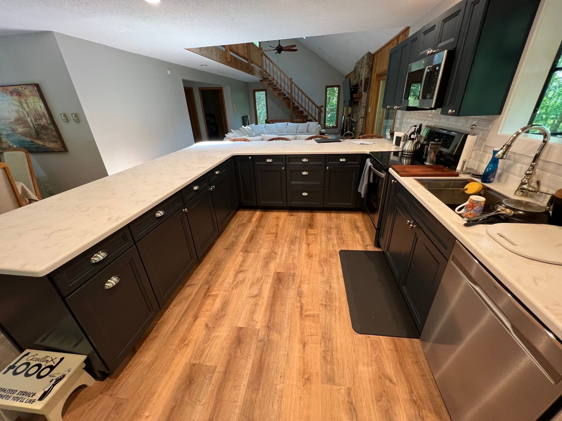 Modern kitchen with dark cabinets, light countertops, stainless appliances, and wood flooring.