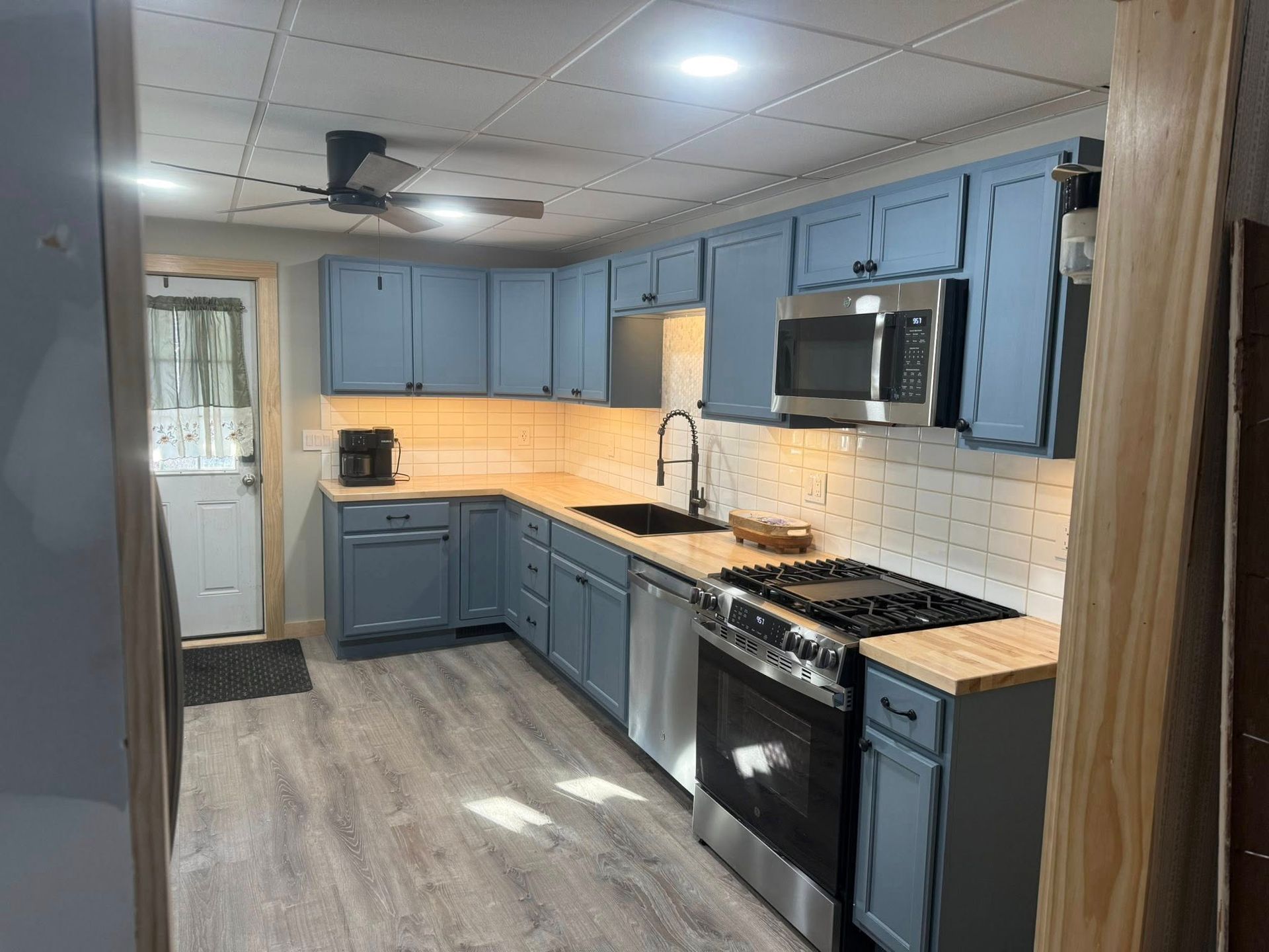 Modern kitchen with blue cabinets, gray floors, stainless appliances, and white tile backsplash