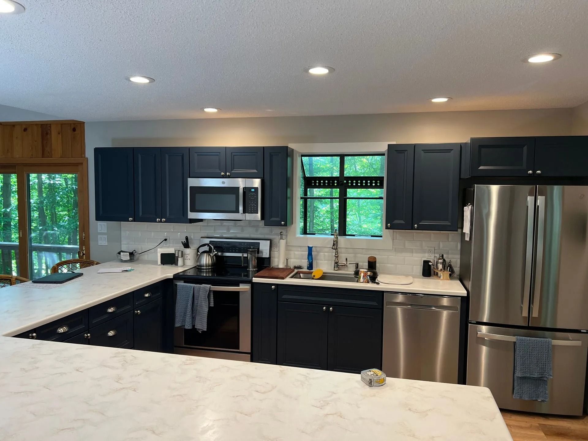 Modern kitchen with dark cabinets, white countertops, stainless steel appliances, and a large island.