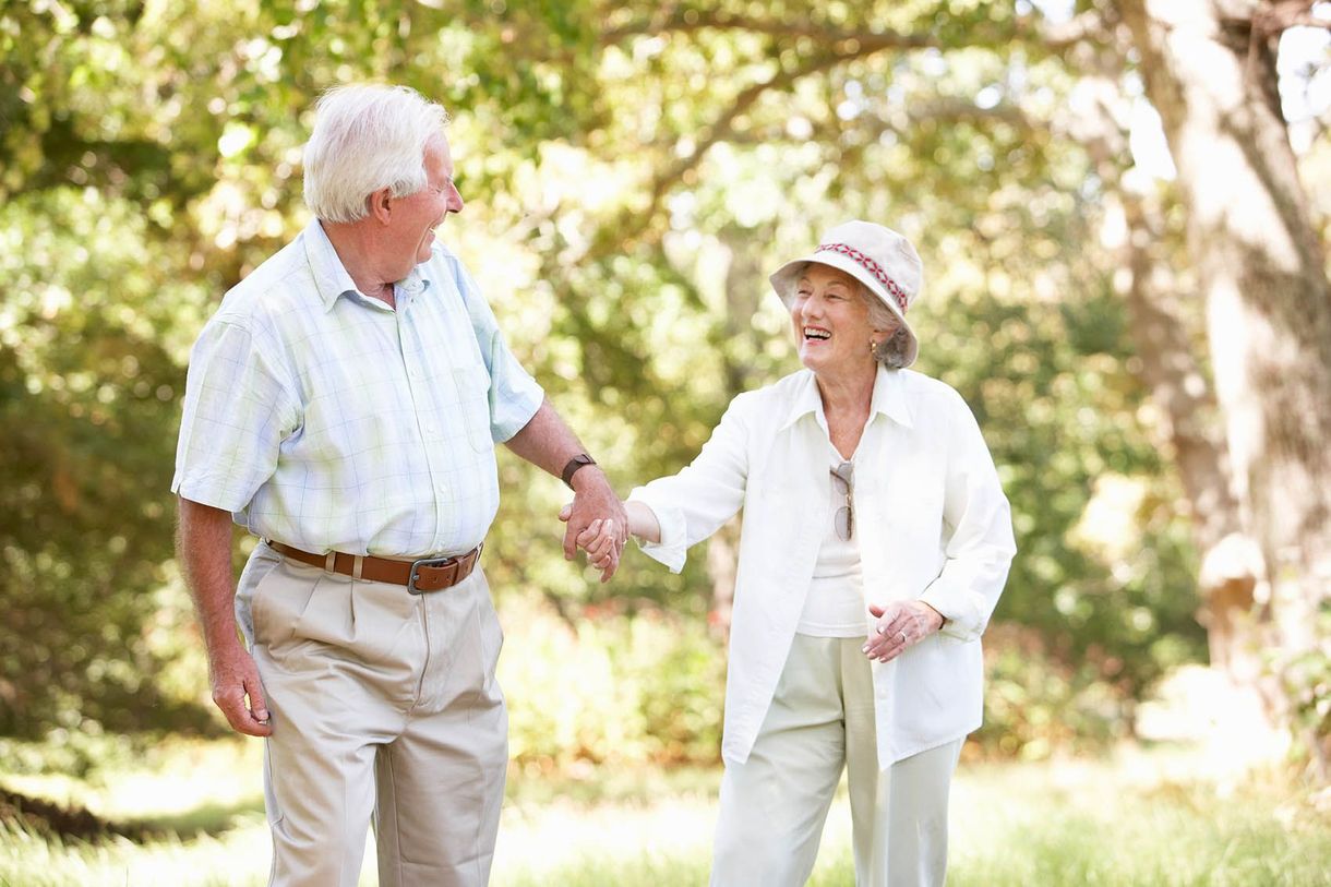 An elderly couple is holding hands while walking in a park.