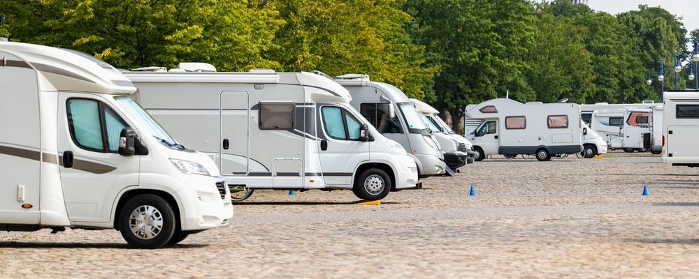 White RVs parked in a gravel lot, trees in the background on a sunny day. — Bay & Basin Storage In Nowra, NSW