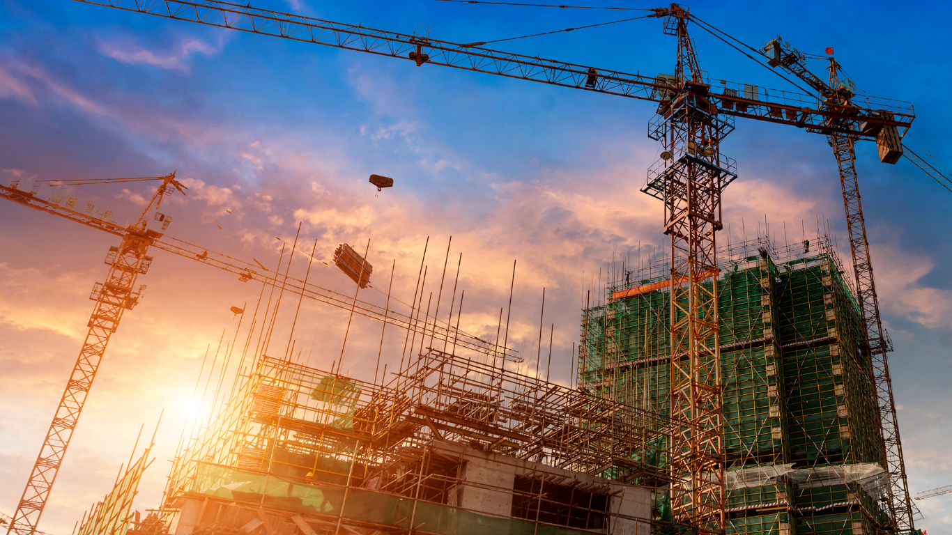 A construction site with cranes and a building under construction at sunset.