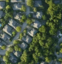 An aerial view of a suburban neighborhood with houses nestled among dense green trees and winding roads.