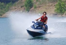 Person riding a blue and white jet ski on a lake, creating a water spray.