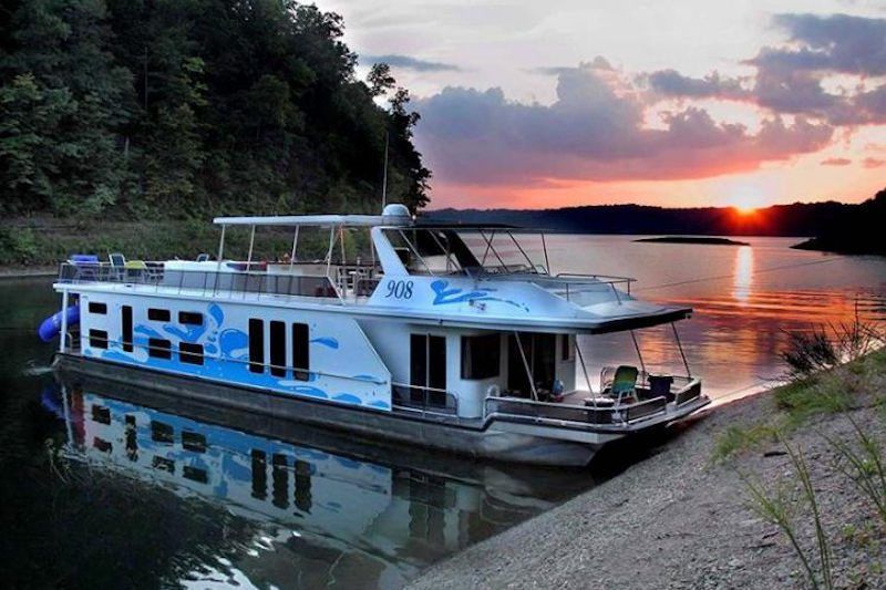 Houseboat on water at sunset with trees in the background. Blue and white paint.