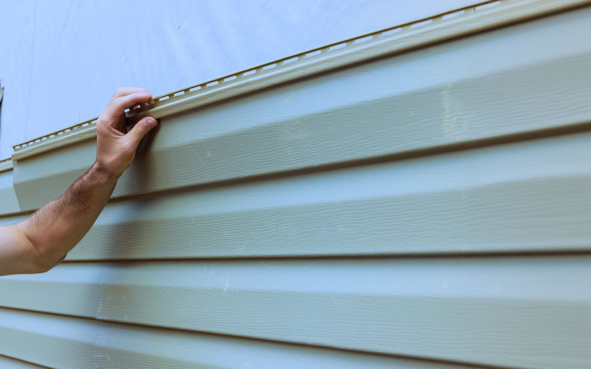 A man is installing siding on a house.