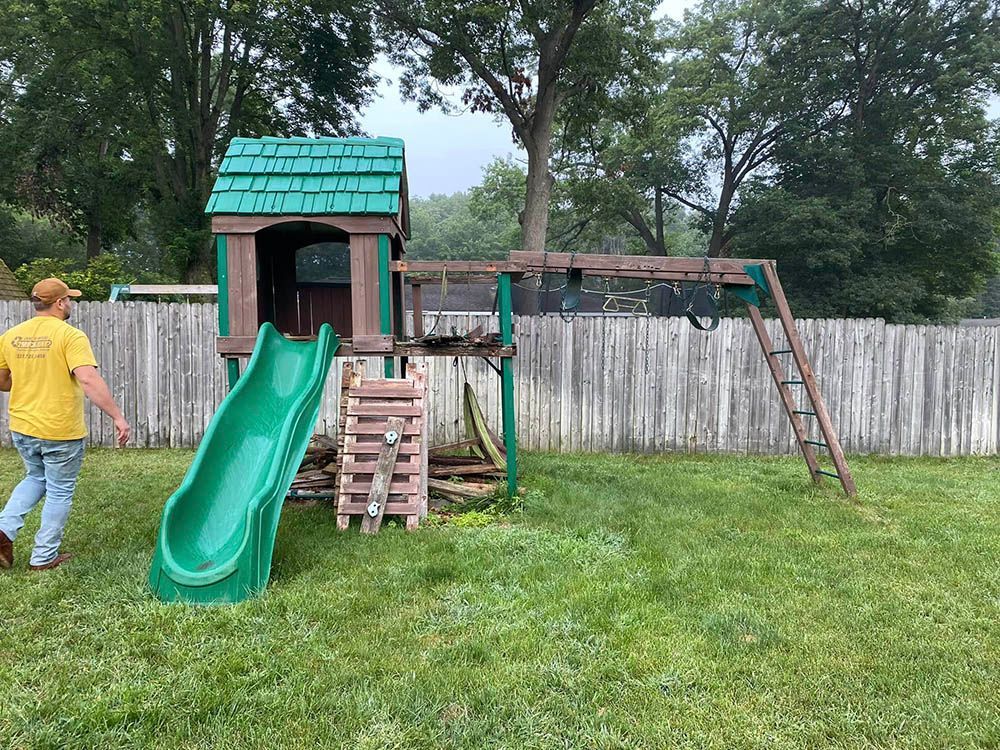 A man is walking in front of a playground with a slide and swings.