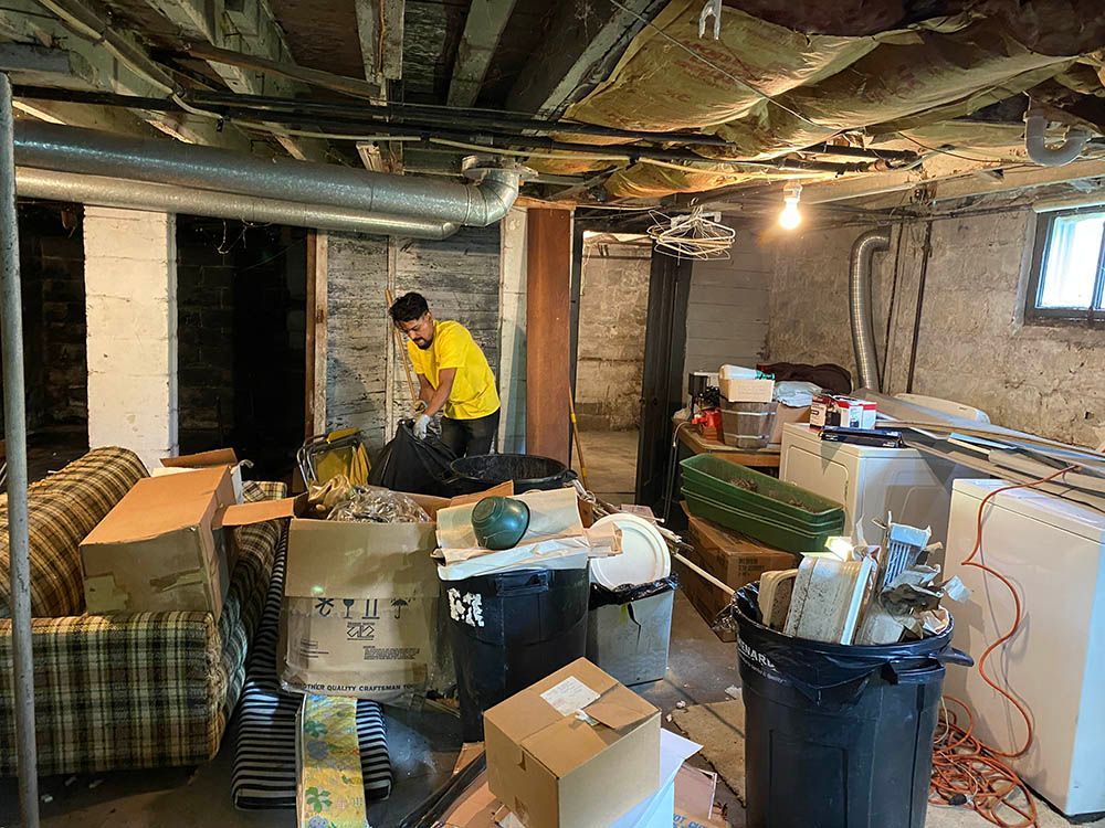 A man is standing in a basement filled with boxes and trash cans.