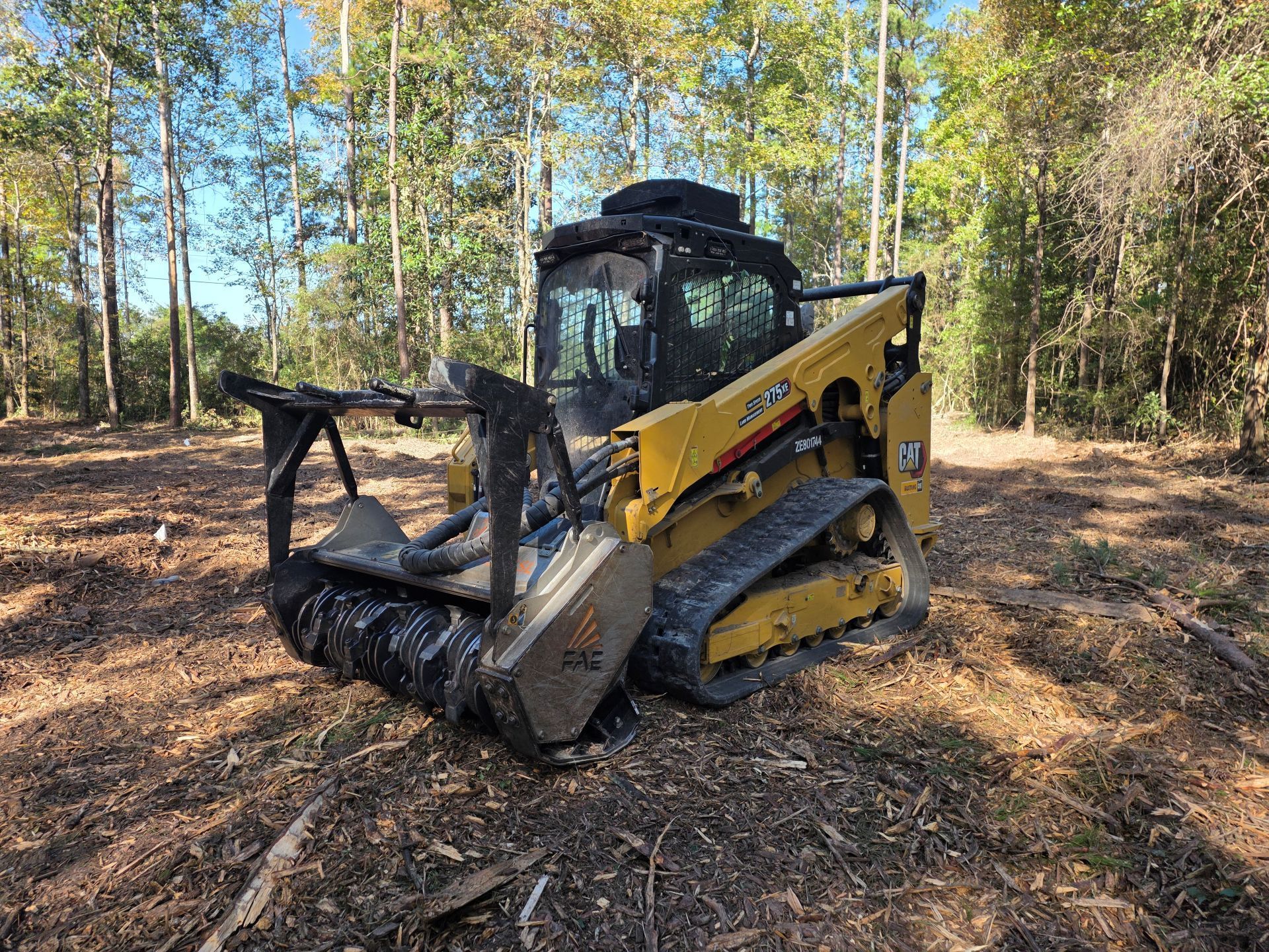 Yellow forestry mulcher on tracks in a wooded area, shredding vegetation.