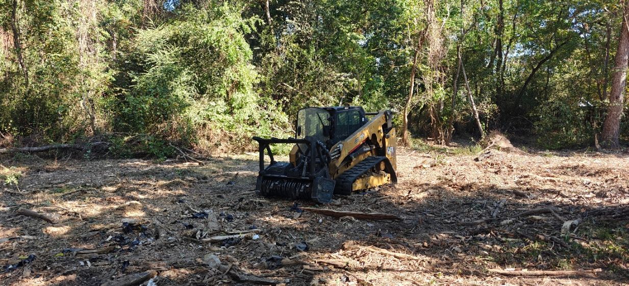 A small bulldozer is in a wooded area with trees in the background.
