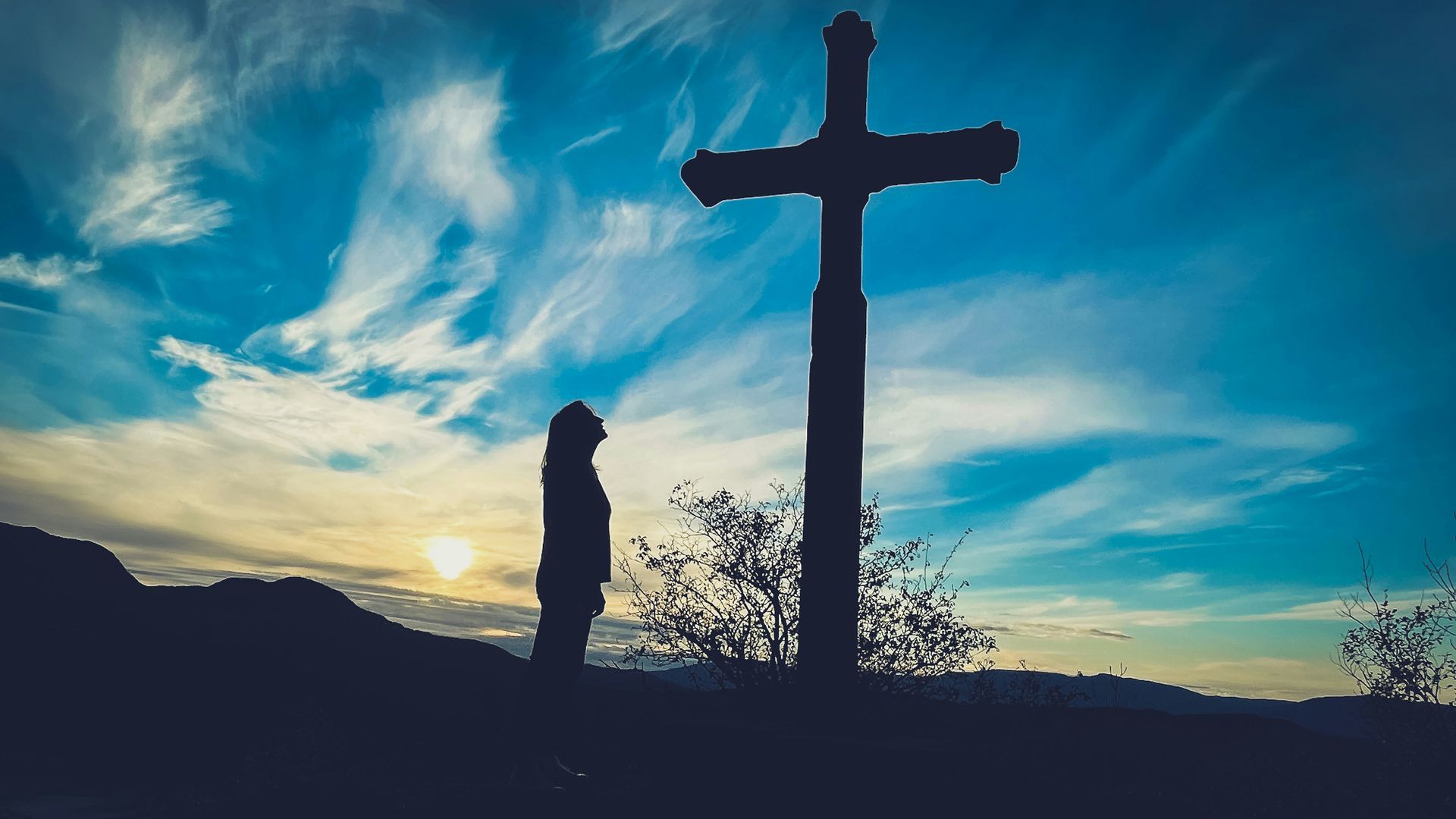 a man is standing in front of a cross at sunset .