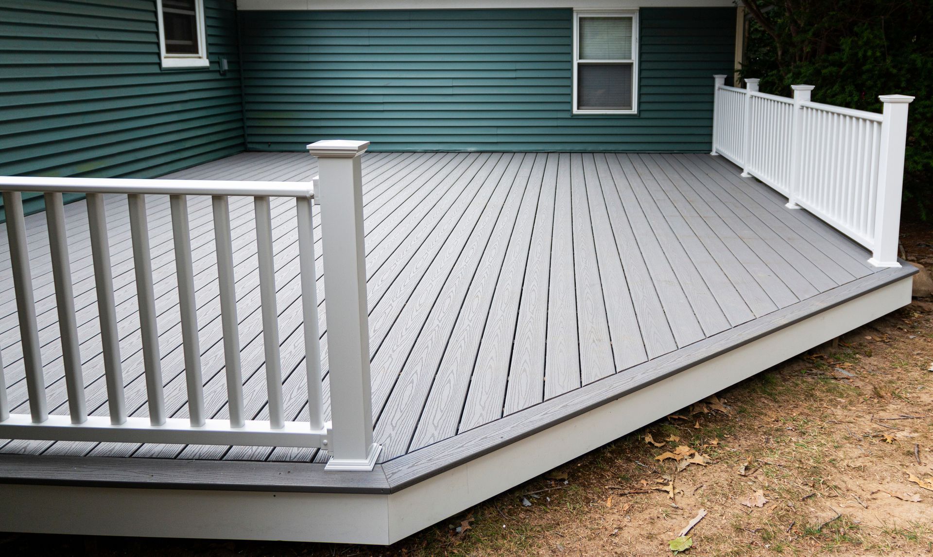Gray composite deck with white railing attached to a teal house.